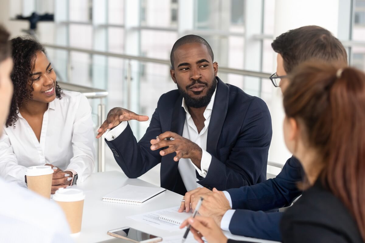 A man speaking with others sitting at a table