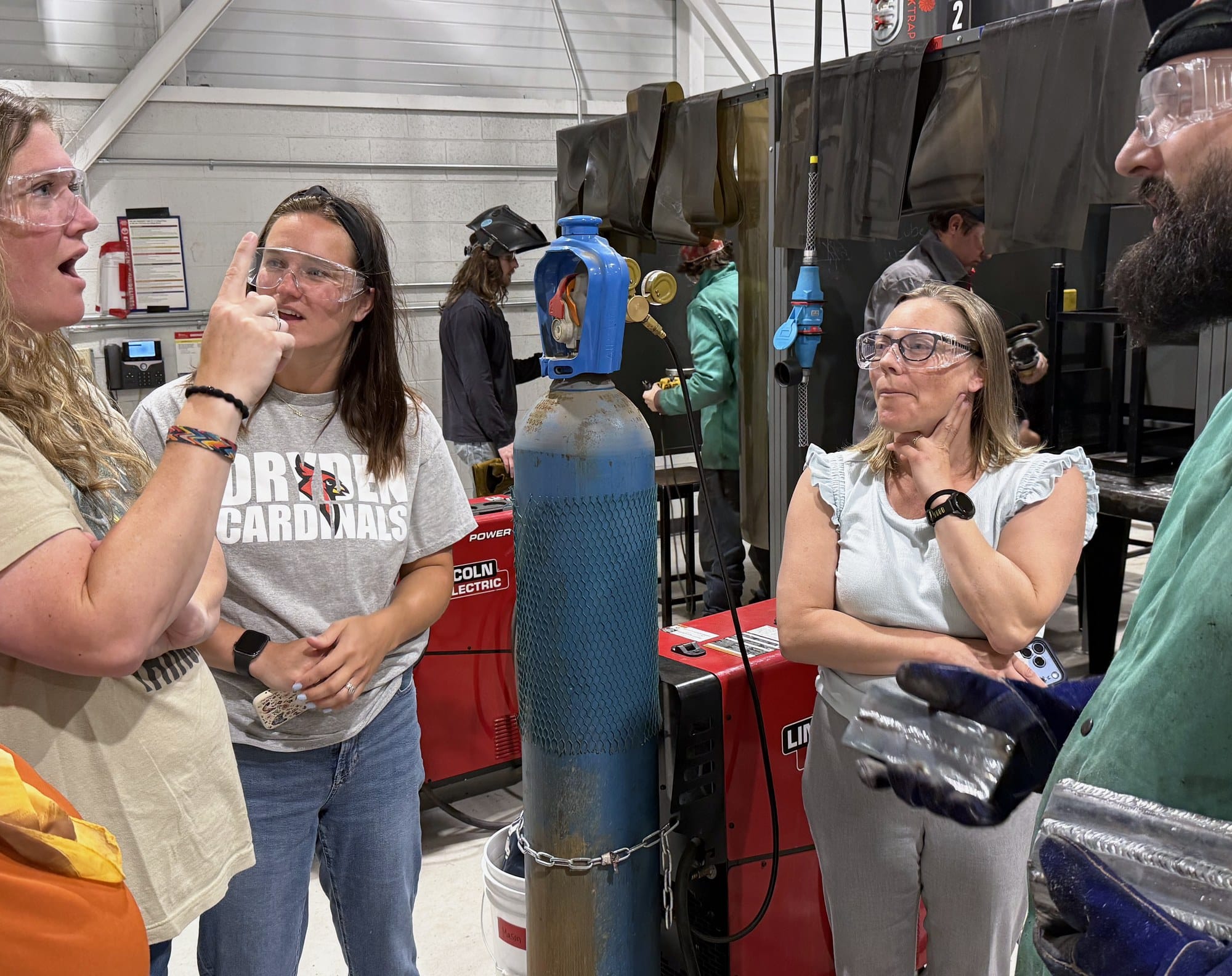 Teachers in safety glasses discuss welding techniques with an instructor during a Battelle Teacher Academy industry externship at a Michigan manufacturing facility.