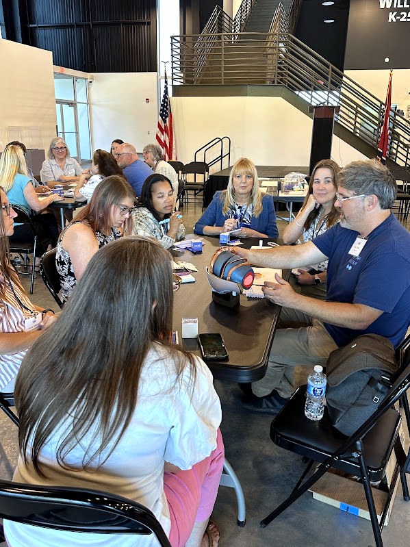 Educators seated around a table examine a tabletop reactor model during a K–2 nuclear energy professional development session.