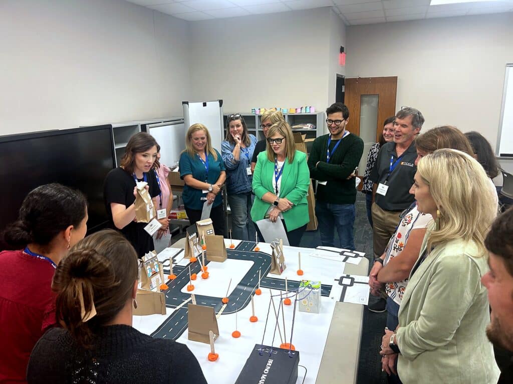 Teachers gather around a model town built on a road-map mat during the “Powering Our Town” curriculum activity.
