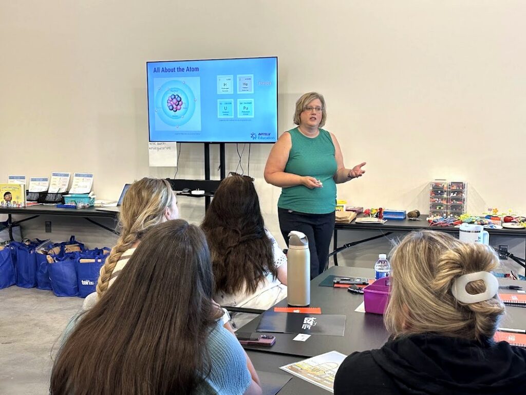 An instructor presents an “All About the Atom” slide to seated teachers at a nuclear energy training workshop.