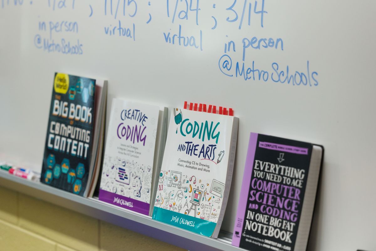 Four books sitting on a shelf in front of a whiteboard