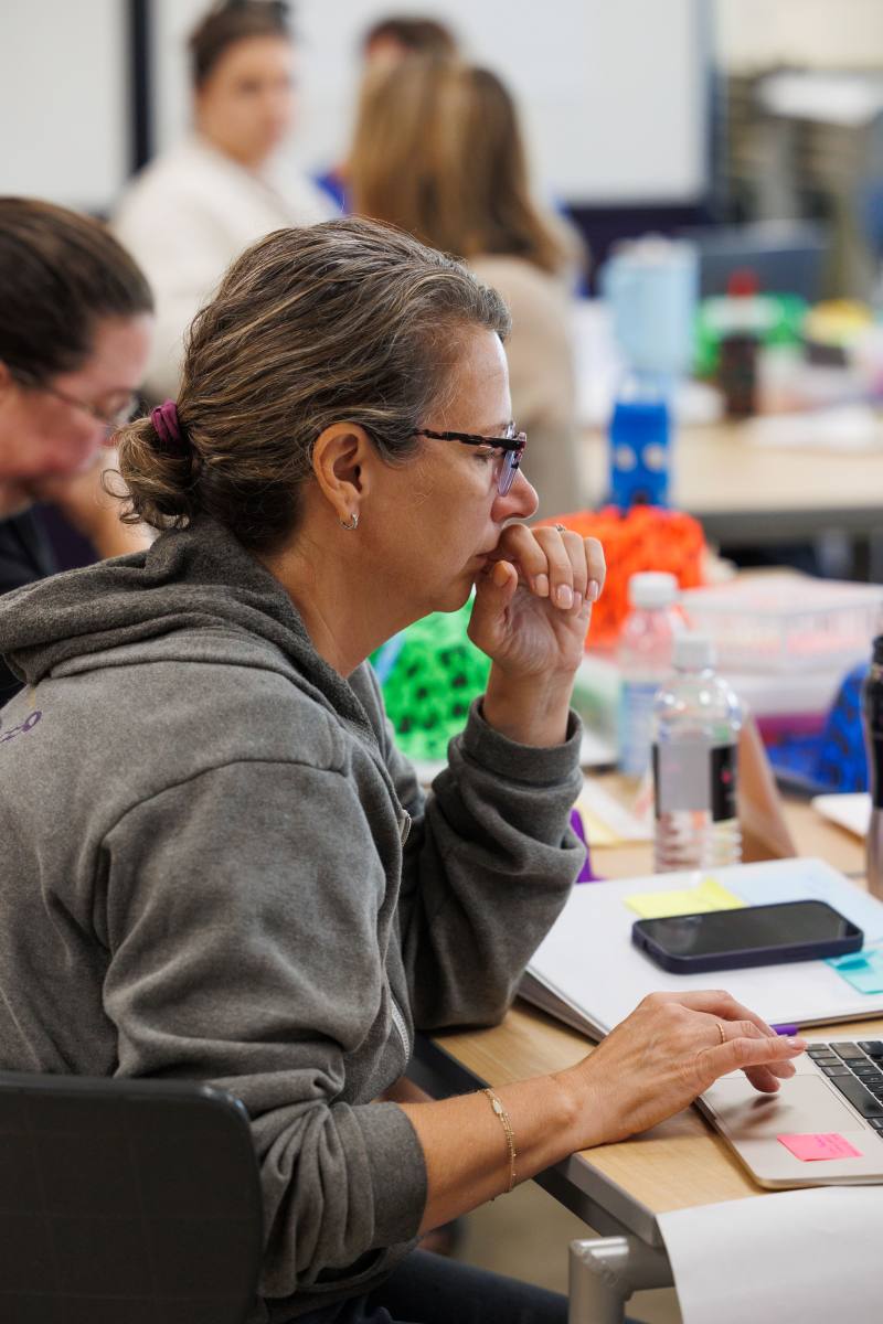 A woman sitting at a table while looking at a laptop