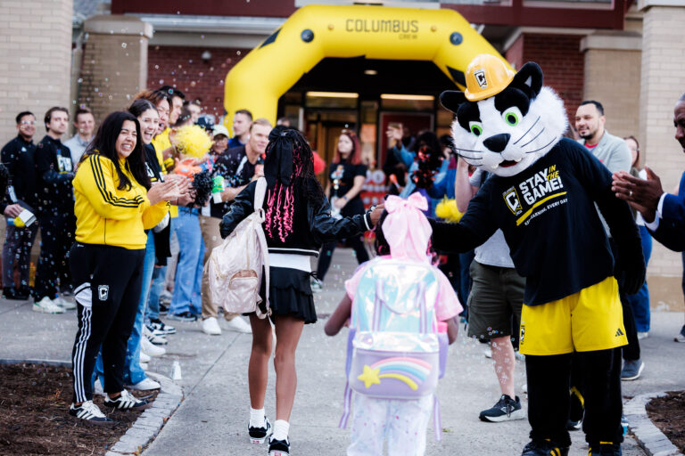 A mascot high fiving young fans
