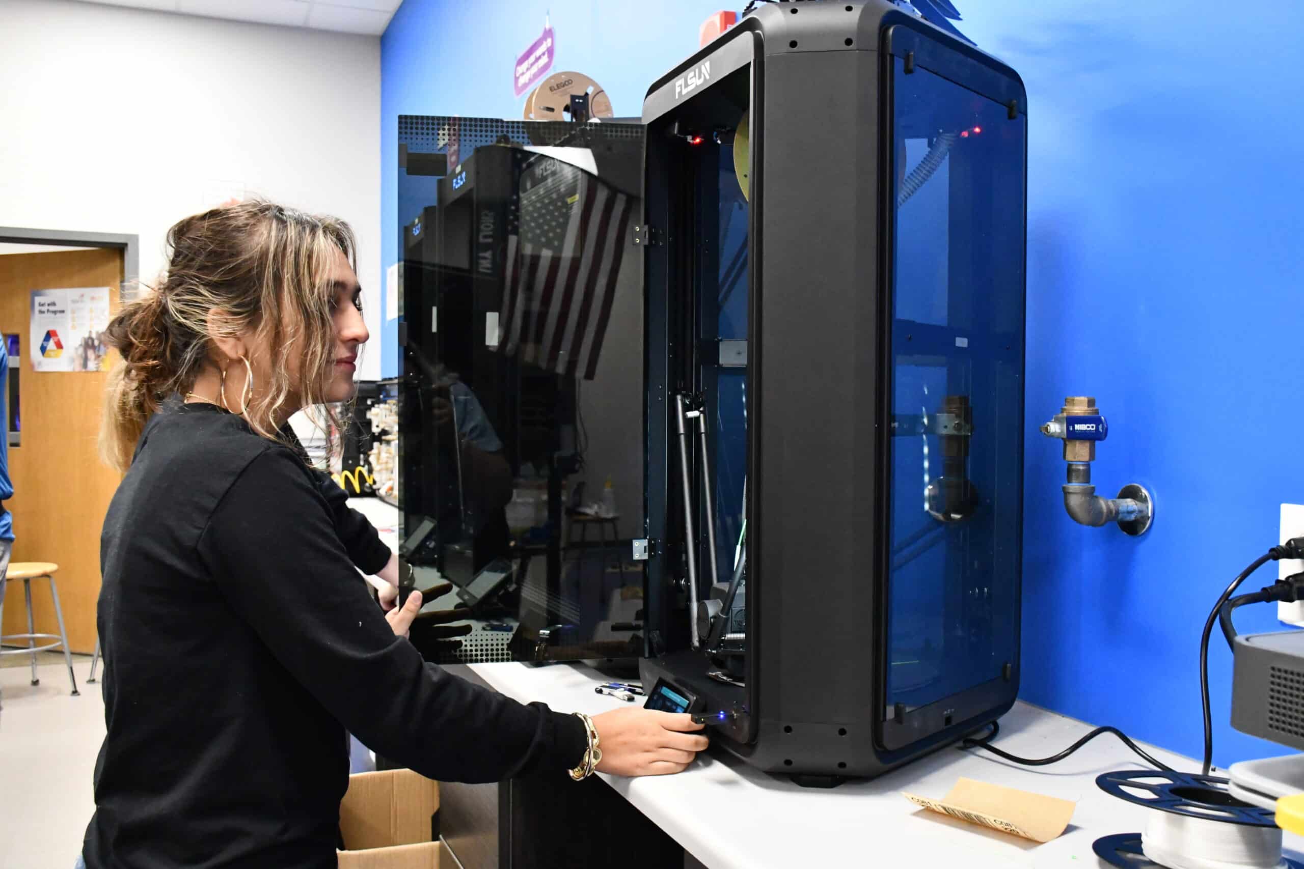 A student operates the control panel of a 3D printer in a classroom fabrication lab.