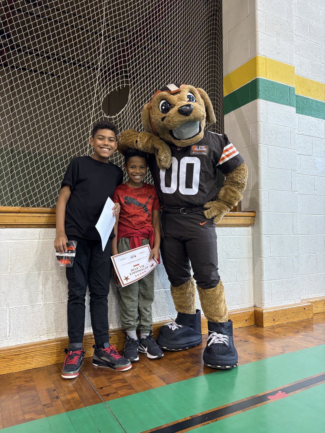 Two Lorain Bilingual Academy students hold an Attendance All-Star certificate beside the Cleveland Browns mascot.