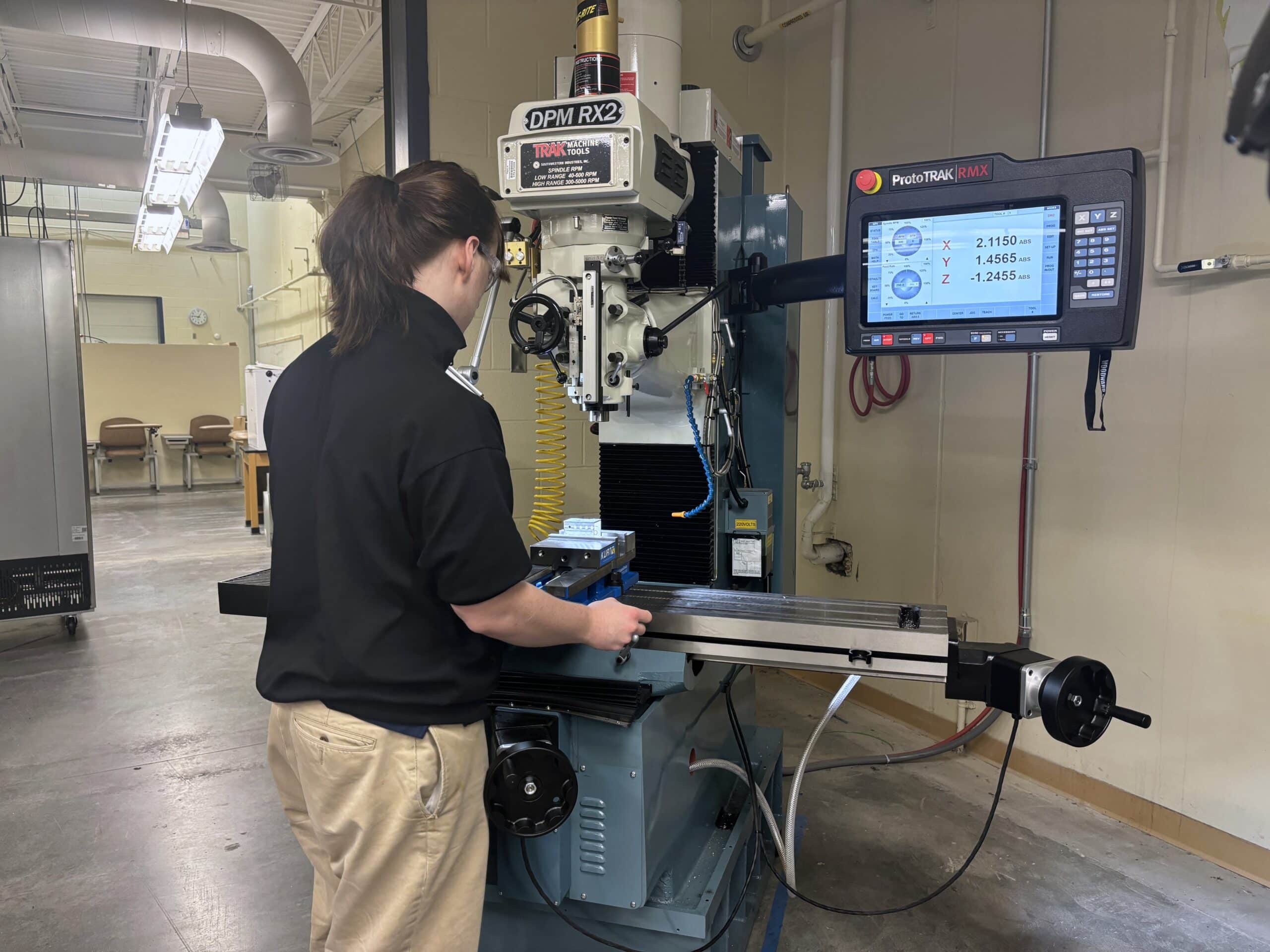 A student operates a CNC milling machine control panel in a manufacturing technology classroom.